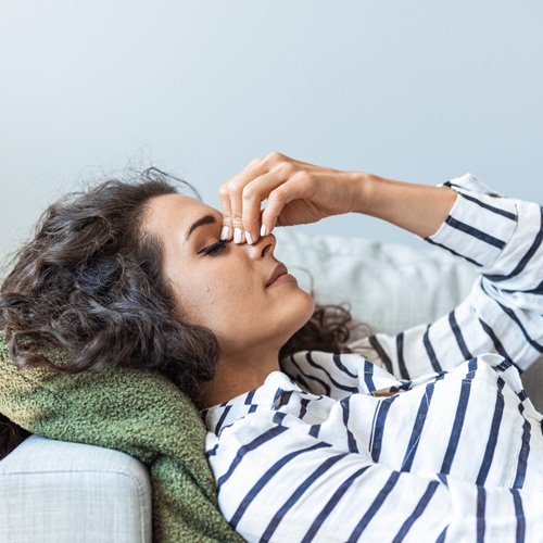 woman relaxing on couch with hand on forehead feeling stress or tension in a cozy room focusing on mindfulness and self-care strategies