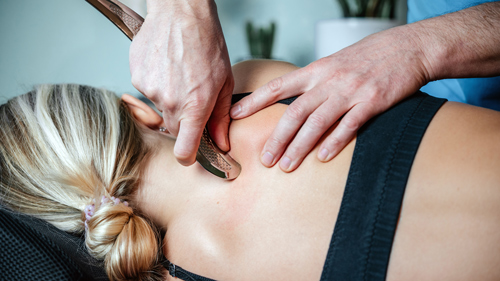 a woman receiving a therapeutic treatment on her back with a hand-held tool highlighting two techniques for pain relief and relaxation